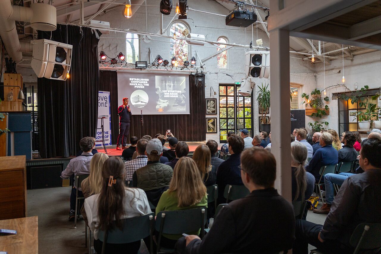 A speaker on stage before a full room at Ingensteds