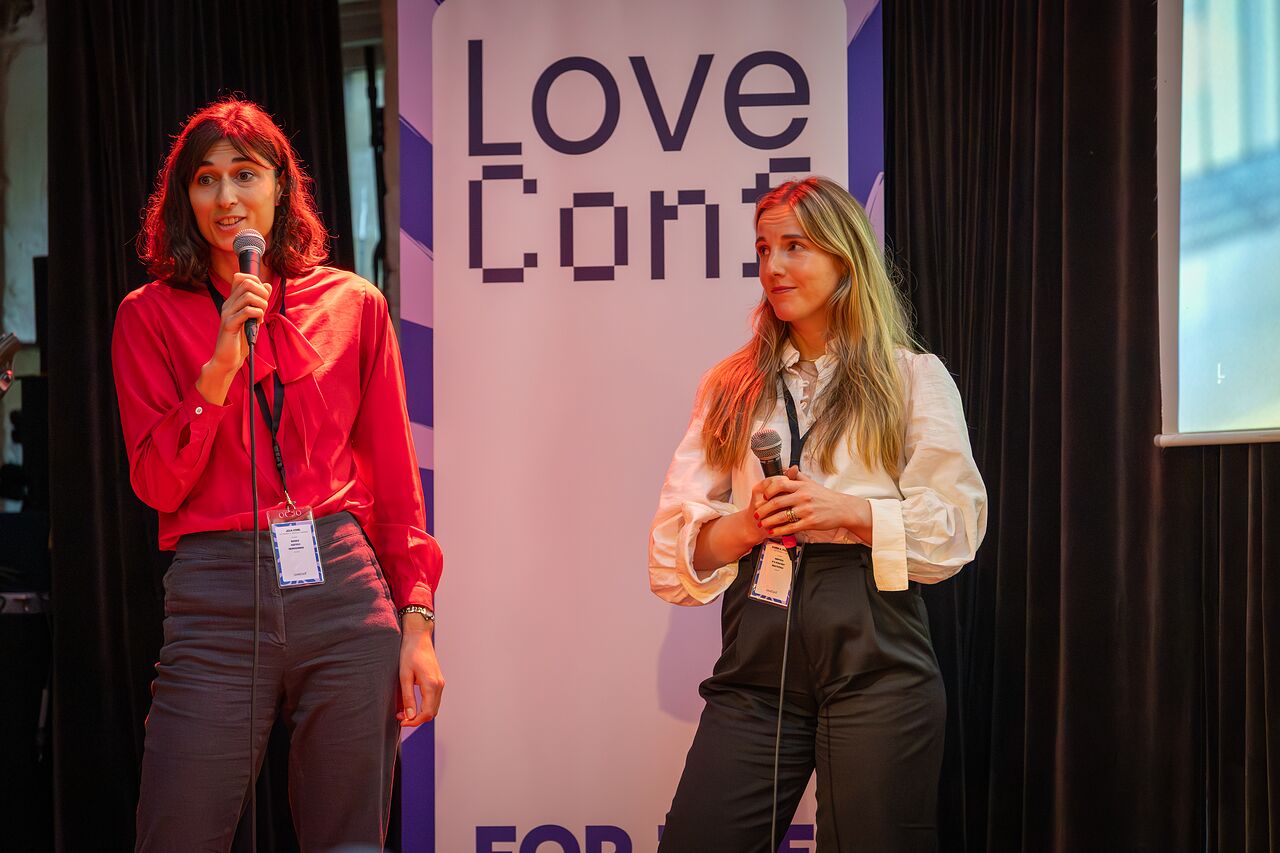 Two speakers on stage in front of the LoveConf banner